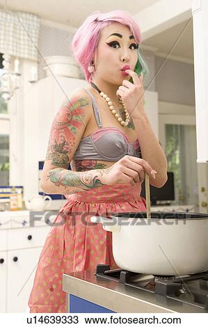 Stock Image - Portrait of a woman licking finger while stirring food on stove. Fotosearch