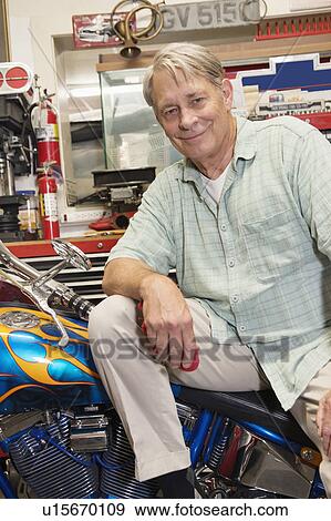 Stock Photo - Portrait of senior man sitting on motorcycle in workshop. Fotosearch