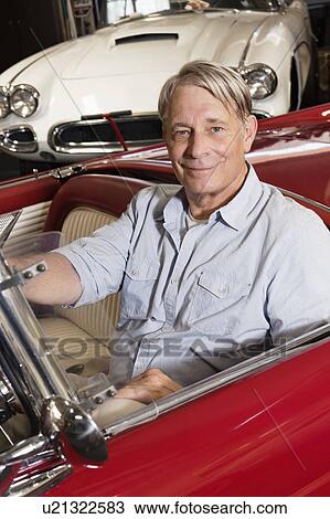 Stock Image - Portrait of smiling elderly man sitting in car in shop. Fotosearch