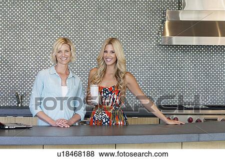 Stock Photo - Portrait of smiling senior mother and daughter standing in kitchen. Fotosearch
