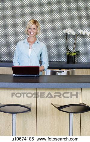 Stock Photography - Portrait of smiling woman using laptop in kitchen. Fotosearch