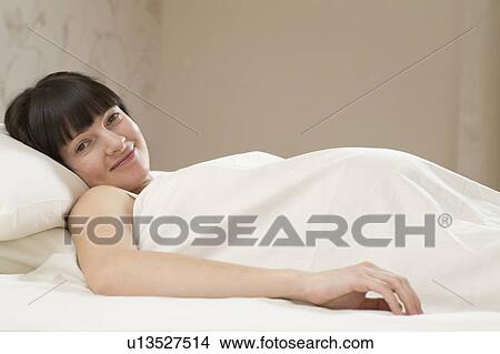 Picture - Portrait of smiling young pregnant woman lying on bed. Fotosearch
