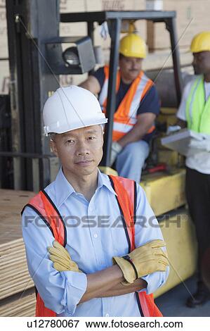 Stock Photo - Portrait of warehouse manager with arms crossed and colleagues in background. Fotosearch