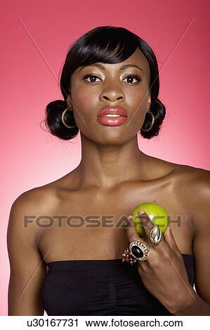 Stock Image - Portrait of young woman holding green apple over colored background. Fotosearch