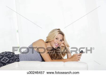 Stock Photo - Portrait of young woman with cell phone lying. Fotosearch