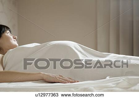 Stock Image - Pregnant woman on bed looking away. Fotosearch