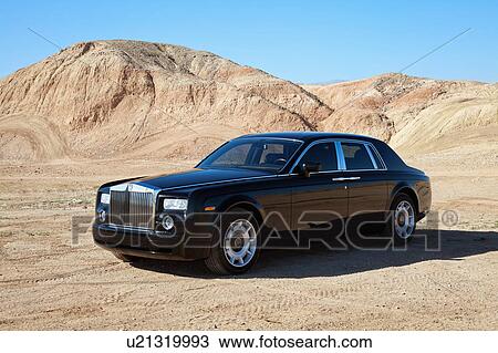 Stock Image - Rolls Royce car parked on unpaved road in front of mountains. Fotosearch