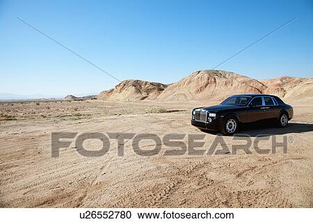Stock Image - Rolls Royce car parked on unpaved road in front of mountains. Fotosearch