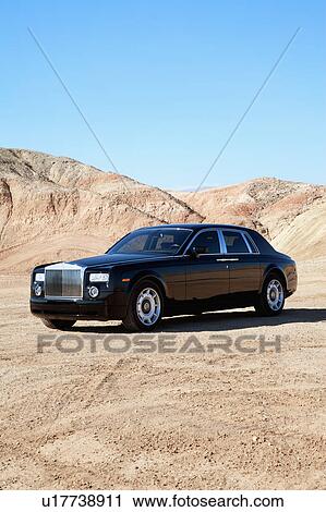 Stock Image - Rolls Royce parked on unpaved road with clear sky. Fotosearch