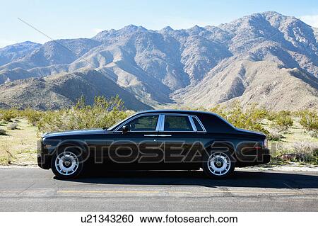 Stock Image - Rolls Royce travelling on country road in front of mountains. Fotosearch