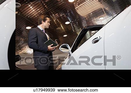 Salesman standing in automobile showroom View Large Photo Image Stock Photo - Salesman standing in automobile showroom. Fotosearch