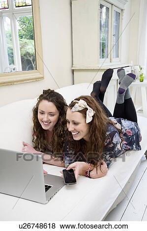 Stock Photo - Siblings sharing laptop on sofa. Fotosearch