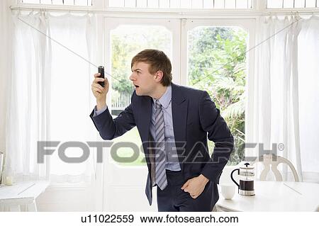 Surprised businessman looking at his cell phone View Large Photo Image Stock Photo - Surprised businessman looking at his cell phone. Fotosearch