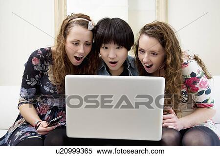 Stock Photography - Surprised friends looking at something in laptop. Fotosearch