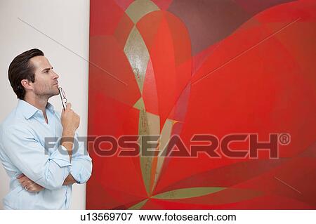 Stock Photo - Thoughtful young man looking at painting in art gallery. Fotosearch