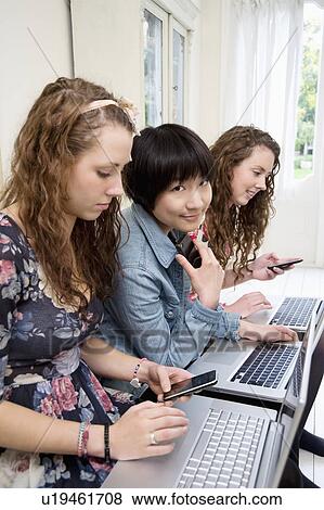 Three female friends using laptop and cell phone View Large Photo Image Stock Photo - Three female friends using laptop and cell phone. Fotosearch