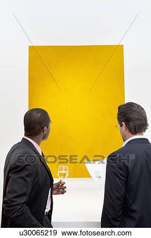 Two people looking at yellow painting on wall in art gallery View Large Photo Image Stock Photo - Two people looking at yellow painting on wall in art gallery. Fotosearch