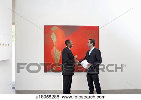 Stock Photo - Two people shaking hands in front of wall painting. Fotosearch