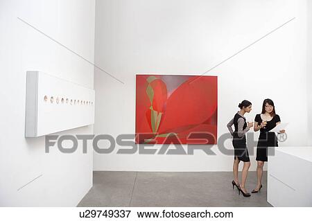 Two woman standing next to wall paintings View Large Photo Image Stock Photo - Two woman standing next to wall paintings. Fotosearch