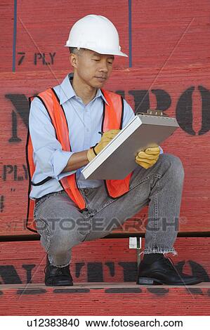 Stock Image - Warehouse manager writing on clipboard. Fotosearch