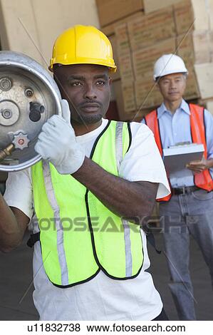 Warehouse worker carrying cylinder with manager in background View Large Photo Image Stock Photo - Warehouse worker carrying cylinder with manager in background. Fotosearch