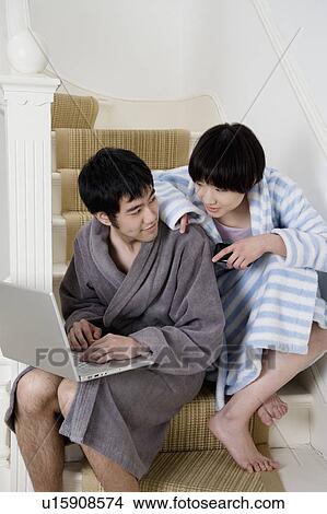 Picture - Young couple in bathrobe sitting on stairway with laptop. Fotosearch