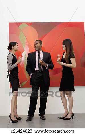 Stock Image - Young executives having a conversation in front of painting in art gallery. Fotosearch