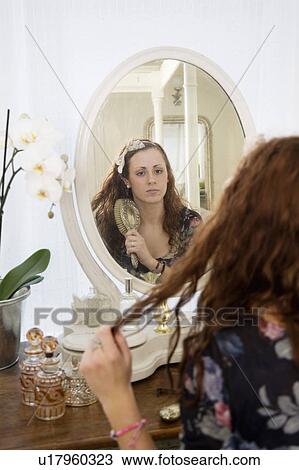 Young woman brushing her hair in front of mirror View Large Photo Image Stock Image - Young woman brushing her hair in front of mirror. Fotosearch