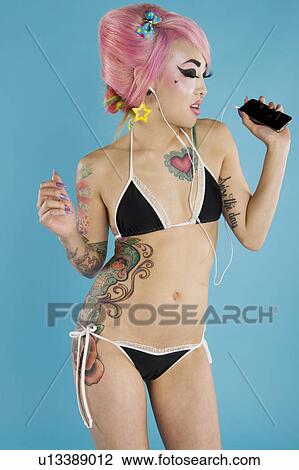 Stock Image - Young woman in bikini listening to music over blue background. Fotosearch