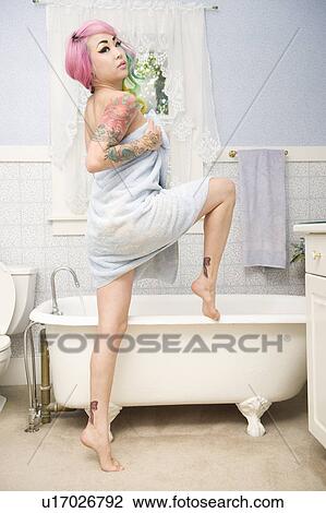 Stock Image - Young woman in towel posing in front of bathtub. Fotosearch