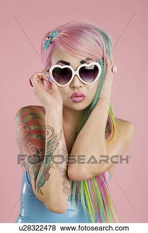 Stock Photo - Young woman posing wearing sunglasses over pink background. Fotosearch