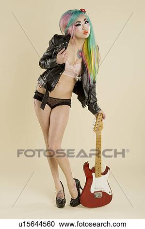 Stock Image - Young woman posing with guitar over colored background. Fotosearch