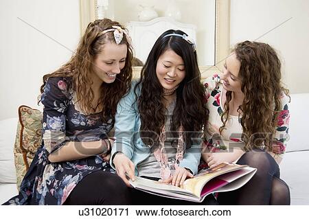 Stock Image - Young women looking at magazines on a sofa. Fotosearch
