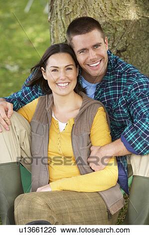 Stock Photograph - Couple sitting against tree trunk. Fotosearch