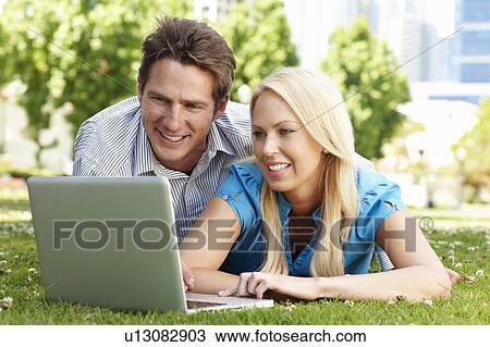 Stock Image - Couple using laptop in city park. Fotosearch