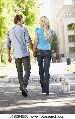 Stock Image - Couple walking with dog in city street. Fotosearch