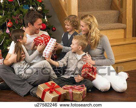 Stock Photograph - Family exchanging gifts in front of Christmas tree. Fotosearch