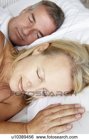 Stock Photograph - Head and shoulders mid age couple sleeping. Fotosearch