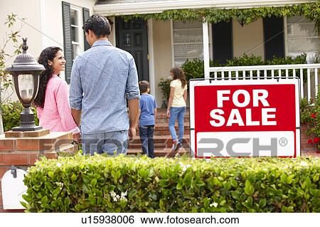 Stock Photograph - Hispanic family outside home with for sale sign. Fotosearch