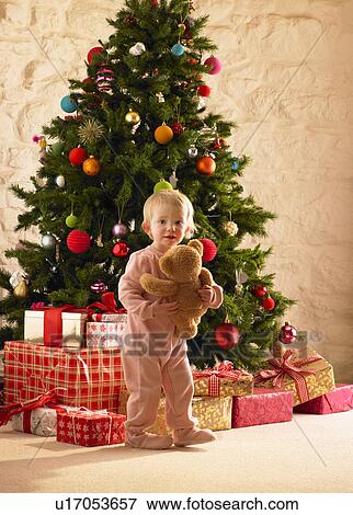 Stock Photo - Little girl with parcels round Christmas tree. Fotosearch