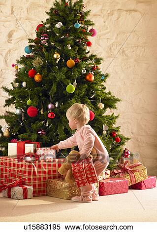 Stock Photography - Little girl with parcels round Christmas tree. Fotosearch