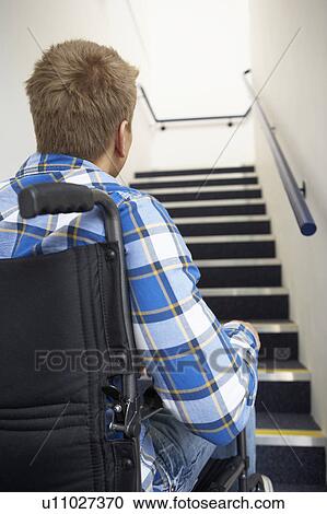 Stock Image - Man in wheelchair at foot of stairs. Fotosearch