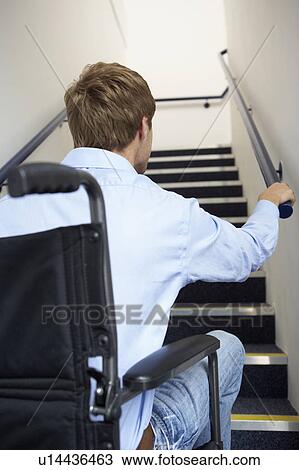 Stock Image - Man in wheelchair at foot of stairs. Fotosearch