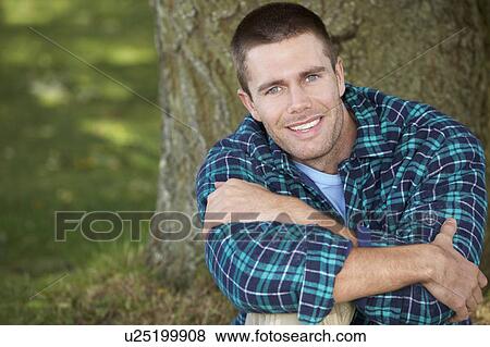 Stock Photo - Man sitting against tree trunk. Fotosearch