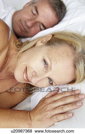 Stock Photo - Mid age couple in bed woman awake. Fotosearch