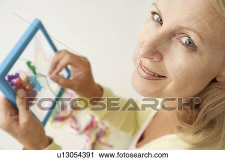 Stock Image - Mid age woman doing cross stitch. Fotosearch