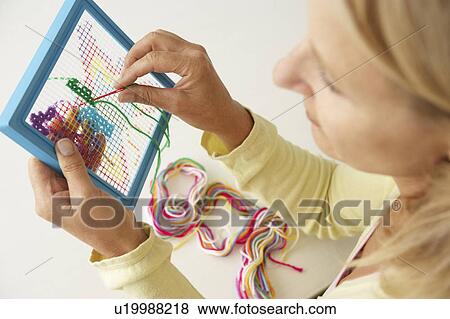 Stock Photo - Mid age woman doing cross stitch. Fotosearch