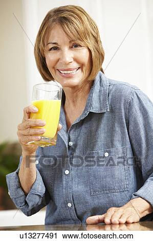 Stock Image - Mid age woman drinking orange juice. Fotosearch