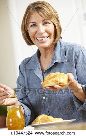 Picture - Mid age woman eating croissants. Fotosearch