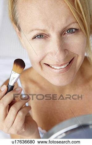 Stock Image - Mid age woman putting on make-up. Fotosearch
